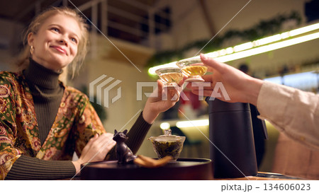 Couple clinking glass tea cups during traditional tea ceremony at wooden table Couple clinking glass tea cups during traditional tea ceremony at wooden table 134606023