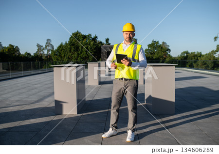 Worker inspecting rooftop solar panels holding digital tablet in hands 134606289