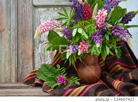 A bouquet of purple and pink lupine flowers in a clay jug on an old wooden background.  134607427