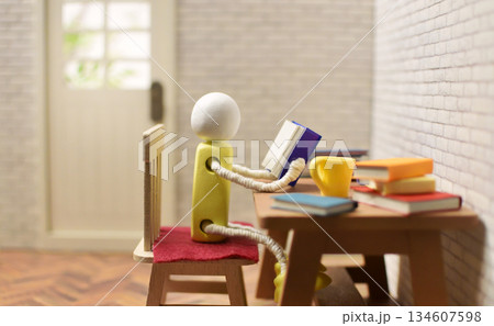 読書をする木製人形の写真　積まれた本　趣味の時間　勉強　ミニチュア 134607598