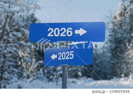 Blue road signs showing 2025 and 2026 with arrows in opposite directions, symbolizing choice, time, new beginnings, and moving forward into the future. Winter forest background. 2026, concept. 134607648