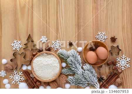 Composition with a snowy spruce branch, flour, eggs, and festive cookie cutters on a wooden table Composition with a snowy spruce branch, flour, eggs, and festive cookie cutters on a wooden table 134607953