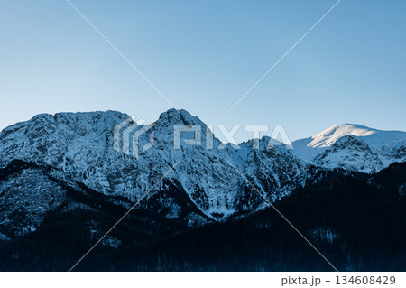 Panoramic view of rugged, snow-covered mountain peaks. Clear winter atmosphere and dark pine slopes. Remote wilderness scenery Panoramic view of rugged, snow-covered mountain peaks. Clear winter atmosphere and dark pine slopes. Remote wilderness scenery 134608429