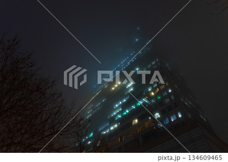 dense grid of office windows lit up at night, highlighting the electrical heartbeat of a financial district. Foggy night cityscape with illuminated office building windows glowing through dense mist. dense grid of office windows lit up at night, highlighting the electrical heartbeat of a financial district. Foggy night cityscape with illuminated office building windows glowing through dense mist. 134609465