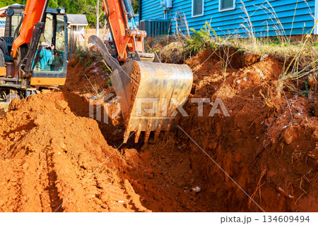 Construction crew works on digging trench with an excavator in yard near house 134609494