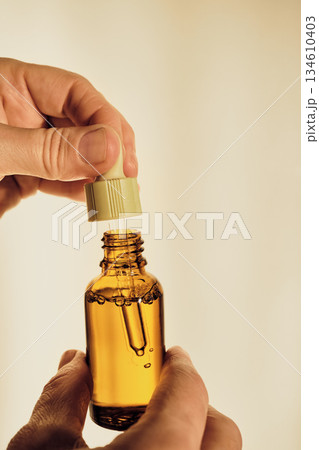 Hands holding an amber bottle with dropper full of essential oil, symbolizing natural skincare 134610403