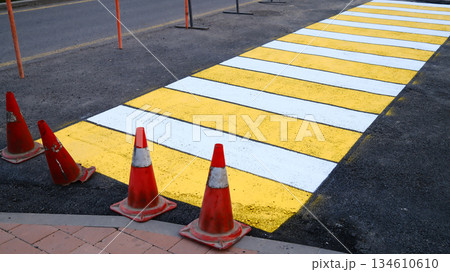 Yellow pedestrian crosswalk with traffic cones on urban road surface 134610610