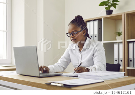 Serious, focused young, beautiful africanamerican girl with glasses, dressed in white shirt. 134612161