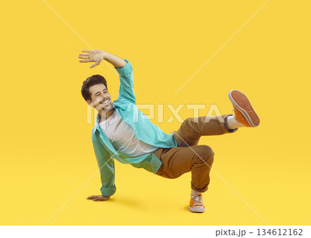 Positive cheerful young casual man funny doing breakdance dance moves isolated on orange background 134612162