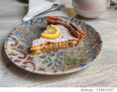 Slice of apple pie served with lemon garnish on patterned plate. Cozy cafe dessert moment, homemade pastry comfort and warm afternoon dining atmosphere. Slice of apple pie served with lemon garnish on patterned plate. Cozy cafe dessert moment, homemade pastry comfort and warm afternoon dining atmosphere. 134612437