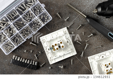 Electrical outlet mounting with screws, driver bits and tools on a dark background. DIY installation and repair concept. Electrical outlet mounting with screws, driver bits and tools on a dark background. DIY installation and repair concept. 134612931