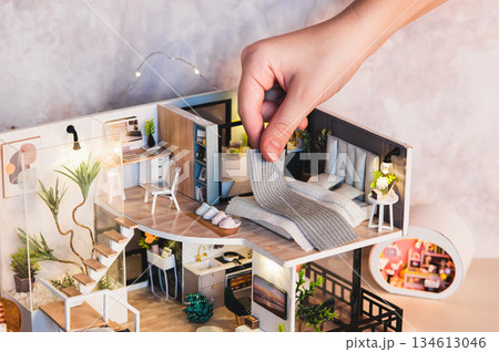 A child's hand puts a blanket on a bed on the second floor of a tiny house on a table 134613046