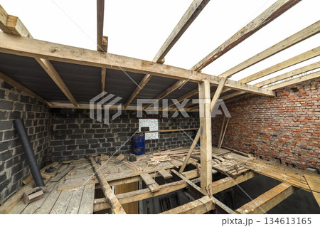 Two-storied building under construction and renovation. Perspective view of energy saving walls of large hollow foam insulation blocks and bricks, temporary wooden scaffolding, beams as roof frame. 134613165