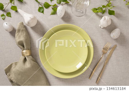 Elegant Easter place setting with pastel green plates, linen napkin, golden cutlery and spring decor on neutral textile background, flat lay composition. 134613184