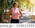 Woman Exercising Outdoors with Earbuds in Sunny Park 134613399
