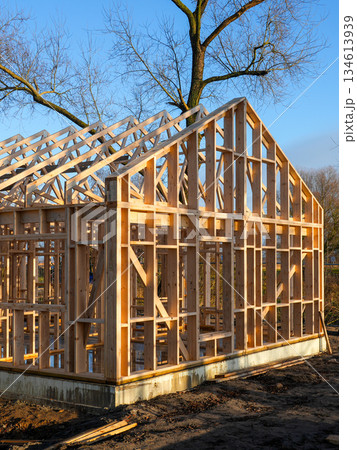 Wooden residential house frame under construction on urban site with blue sky and sunlight 134613939