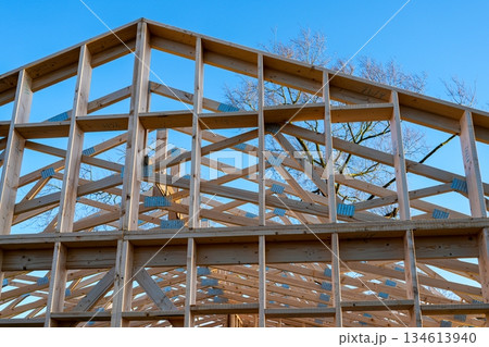 Wooden house roof truss and timber frame under construction against clear blue sky 134613940