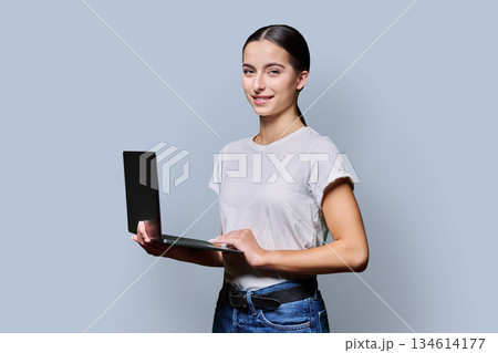 Portrait of smiling teenage girl using laptop on gray studio background 134614177