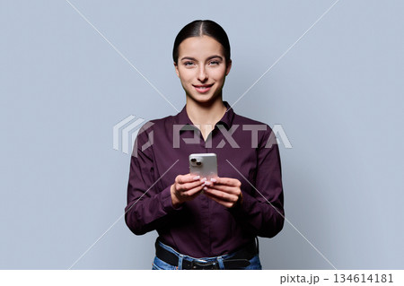 Portrait of smiling teenage girl holding smartphone on gray studio background 134614181