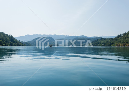 Scenic view of Lake Bled with calm blue water, surrounded by green hills and distant mountains under a clear sky, capturing the beauty of nature and peaceful travel destinations. Old church 134614219