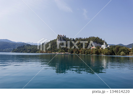 Amazing view of Bland lake with hills, forest, rocks with a castle and a church on the mountain. Travel in Slovenia. Clear water in the lake and mountain landscape Amazing view of Bland lake with hills, forest, rocks with a castle and a church on the mountain. Travel in Slovenia. Clear water in the lake and mountain landscape 134614220