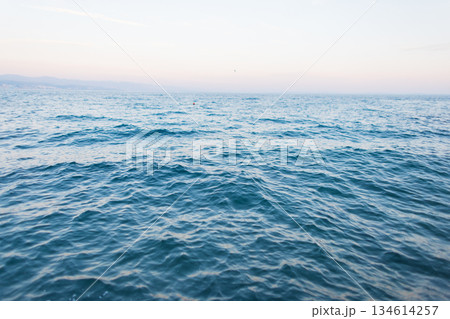 Calm blue sea with gentle waves under a clear sky at sunset. Minimal seascape background symbolizing peace, freedom. Blue ocean surface with calm waves fading into the horizon. Natural seascape 134614257