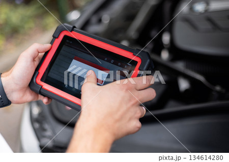 Hands holding a modern car diagnostic tool during vehicle inspection. Mechanic using a digital diagnostic scanner to check car systems inside the vehicle. Hands holding a modern car diagnostic tool during vehicle inspection. Mechanic using a digital diagnostic scanner to check car systems inside the vehicle. 134614280