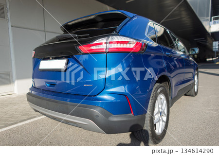 Modern blue SUV parked on city street near concrete building, rear view with tail lights. Compact modern crossover car in blue color, rear view with detail. 134614290
