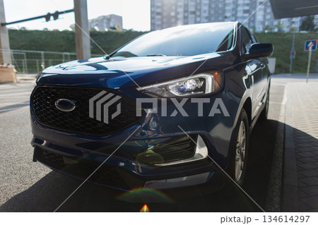 Modern blue SUV parked in the city street, showcasing sleek design, stylish headlights, and urban lifestyle transportation concept with contemporary architecture in the background. 134614297