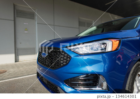 Close-up of a blue SUV front with shiny headlights and hexagon grille, urban background. 134614301