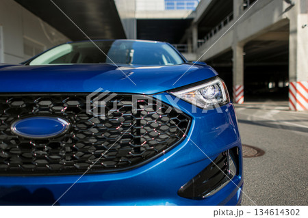 New urban SUV design with futuristic headlights and elegant front exterior. Blue SUV vehicle parked in city parking area near modern wall, side profile view. 134614302