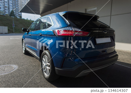 Stylish blue crossover vehicle outdoors, urban architecture background. Sleek blue car parked near concrete structure, rear lights visible. 134614307