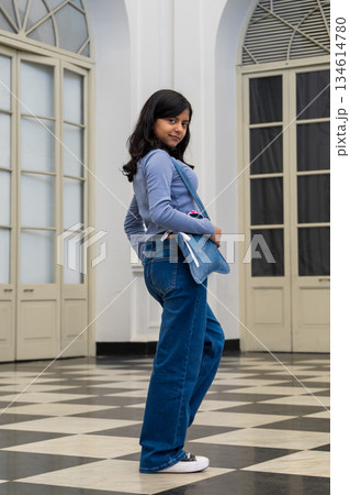 A teen in blue jeans and a striped shirt is posing for a photo A teen in blue jeans and a striped shirt is posing for a photo 134614780