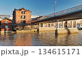 Porvoo, Finland - December 08, 2020: Historic red brick building stands by the river, with a modern bridge overhead, showcasing architectural contrast and scenic waterfront views 134615171