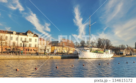 Porvoo, Finland - December 08, 2020: Historic ship is docked by the waterfront, surrounded by buildings and trees, under a clear blue sky with wispy clouds Porvoo, Finland - December 08, 2020: Historic ship is docked by the waterfront, surrounded by buildings and trees, under a clear blue sky with wispy clouds 134615172