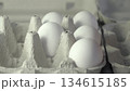 A close-up view of fresh white eggs nestled in a cardboard carton, showcasing their smooth texture and subtle shadows, creating a serene and minimalist atmosphere in the composition 134615185