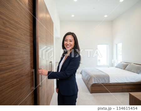 realtor stands in a bright bedroom showing a closet to clients. The space has modern furniture and large windows. They look engaged in conversation about the property. realtor stands in a bright bedroom showing a closet to clients. The space has modern furniture and large windows. They look engaged in conversation about the property. 134615454