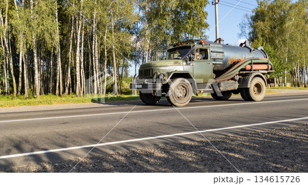 Retro tanker truck travels along an asphalt road through the forest. Delivering fuel for agricultural machinery during the harvest. 134615726