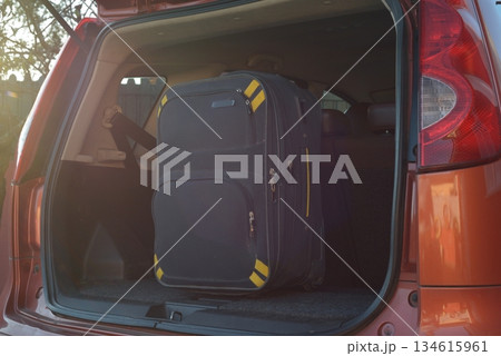 Large black suitcase with yellow accents standing upright inside the trunk of an orange car, ready for a trip. Large black suitcase with yellow accents standing upright inside the trunk of an orange car, ready for a trip. 134615961