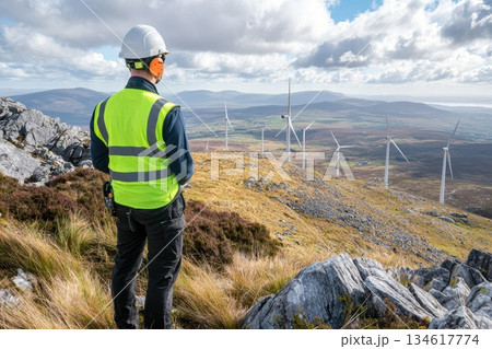 Technician in Neon Green Vest at Wind Farm Overlooking Scenic Landscape Technician in Neon Green Vest at Wind Farm Overlooking Scenic Landscape 134617774