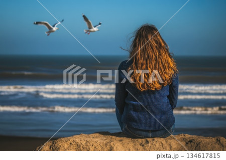 Woman Enjoying Ocean View with Gulls Soaring Above on a Bright Sunny Day 134617815