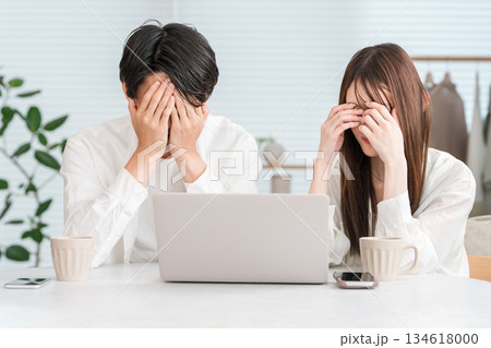 自宅のリビングでパソコンを見ながらショックを受ける若い夫婦,カップル 自宅のリビングでパソコンを見ながらショックを受ける若い夫婦,カップル 134618000