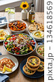 A vibrant spread of plant based meals featuring colorful garden salad, baked sweet potato, chickpea dip, quinoa pilaf, savory tarts, grilled cheese, and refreshing lime water. 134618569