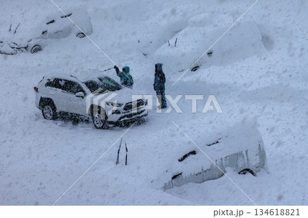 大雪の中で車の雪下ろしを行う人の作業風景 134618821
