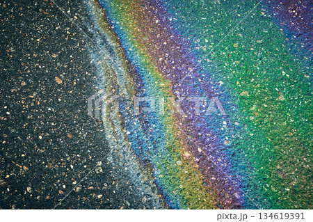 Iridescent oil slick pooling on dark asphalt creating a vibrant rainbow pattern Iridescent oil slick pooling on dark asphalt creating a vibrant rainbow pattern 134619391