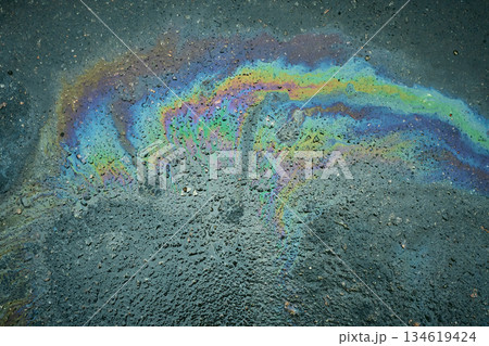 A puddle of gasoline shimmers with bright rainbow reflections on dark asphalt A puddle of gasoline shimmers with bright rainbow reflections on dark asphalt 134619424