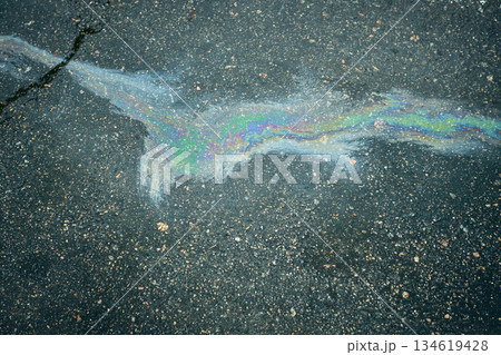 An iridescent puddle of gasoline, reflecting vibrant colors on the rich texture of dark asphalt. 134619428