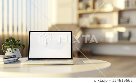 White screen laptop at a round table on wooden floor of living room with large bookshelf or library. 134619665