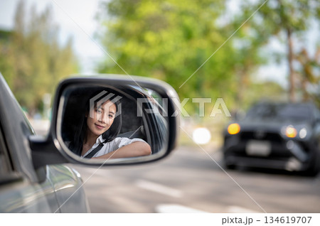 Side mirror shot of smiling asian woman in white shirt, driver of a car parked at lot or roadside. Side mirror shot of smiling asian woman in white shirt, driver of a car parked at lot or roadside. 134619707