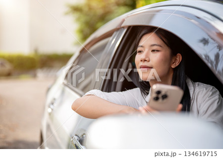 Asian woman in white shirt looking away from phone inside a car parked at parking lot or roadside. 134619715